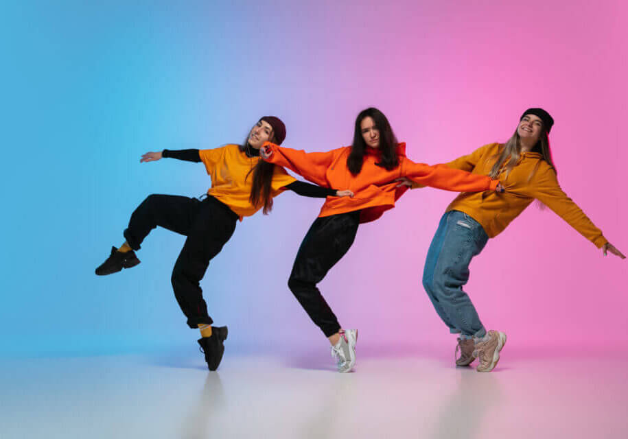 Beautiful sportive girls dancing hip-hop in stylish clothes on colorful gradient studio background in neon light. Youth culture, movement, style and fashion, action. Fashionable bright portrait.